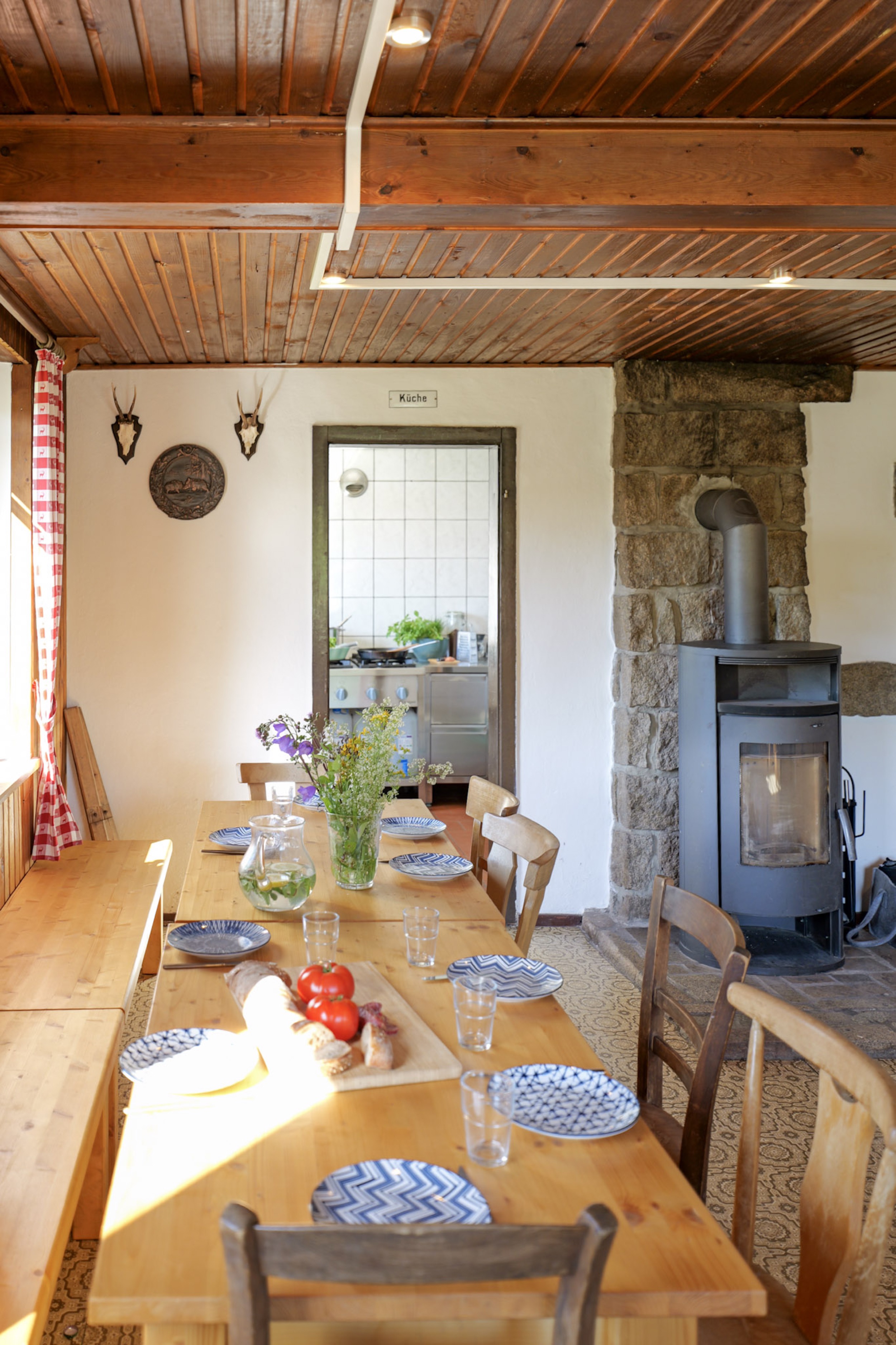 bergwacht-esszimmer-langer-holztisch-mit-blumen-und-kaminofen