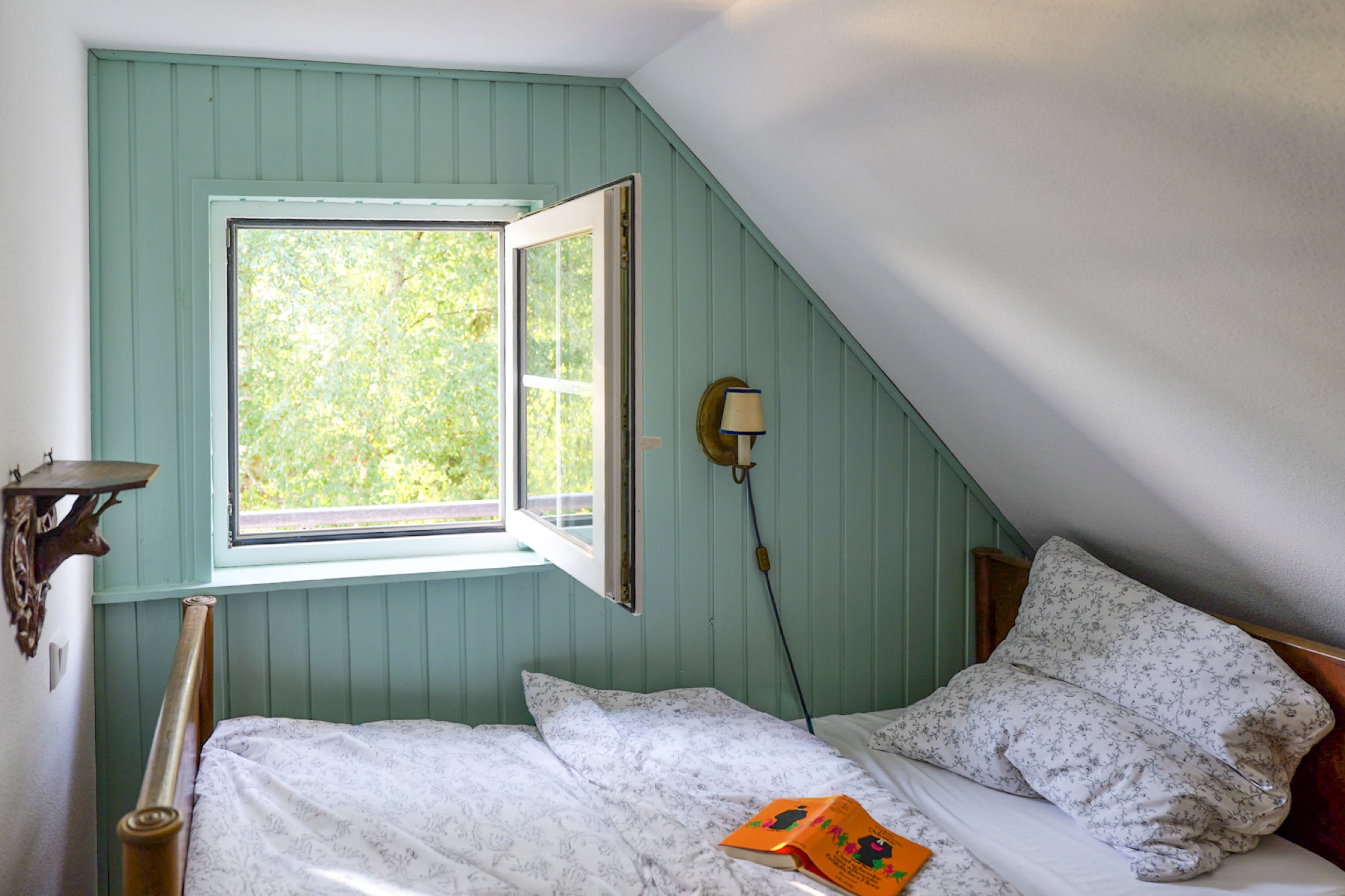 hexenhaus bett unter der dachschraege am offenen fenster mit bettpfosten und bilderbuch