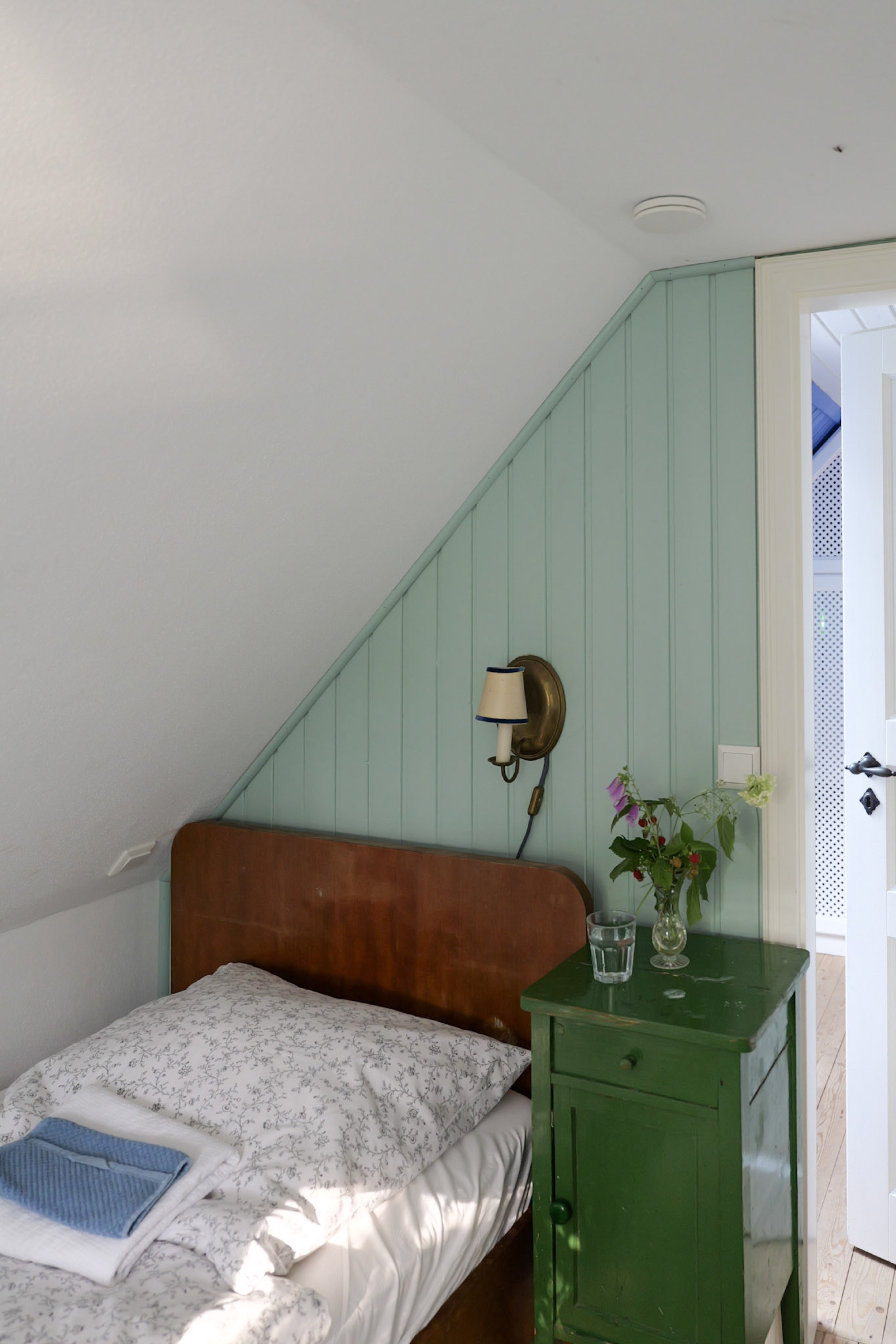 hexenhaus-nachttisch-mit-blumenstrauss-und-blick-durch-die-tuer-zur-veranda-mit-gitterwerk