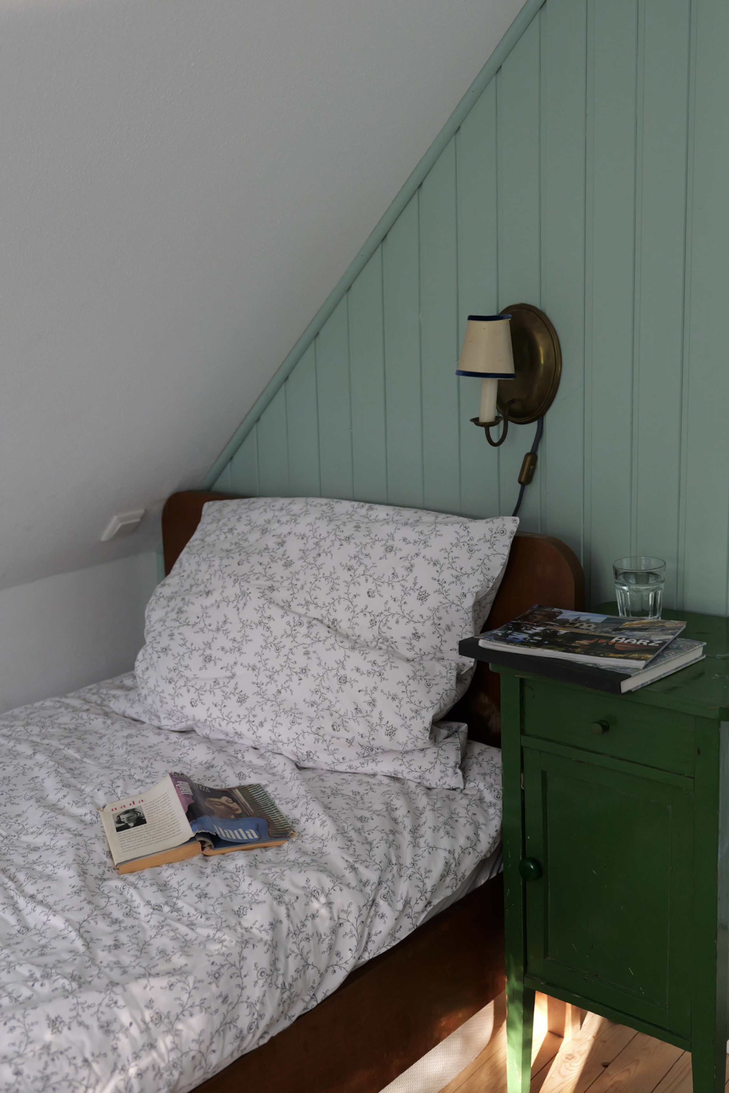 hexenhaus-nachttisch-mit-harz-reisefuehrer-wasserglas-und-aufgeschlagener-zeitschrift-auf-dem-bett